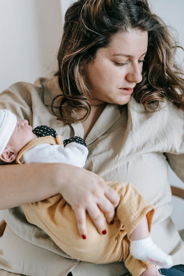 A mother lovingly cradles her sleeping newborn indoors, showcasing warmth and affection.