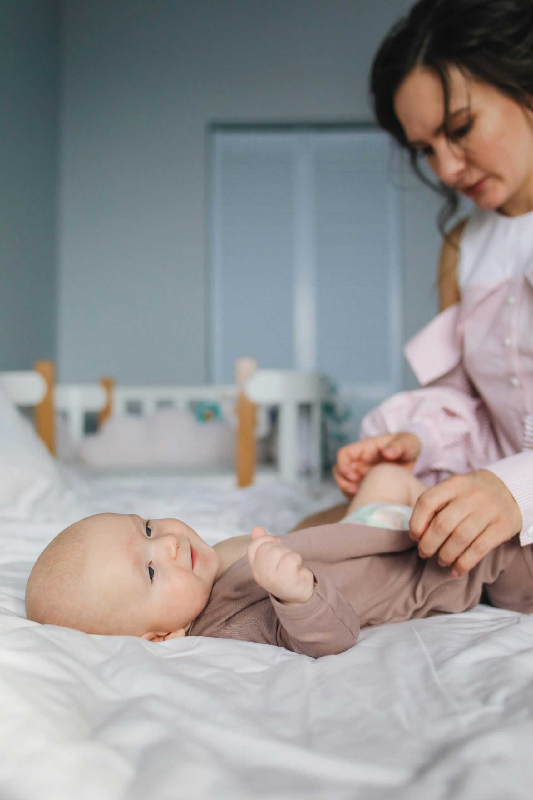 A mother lovingly changes her baby's clothes on a bed in a cozy bedroom setting.