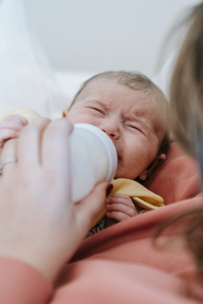 Close-up of a mother feeding her crying newborn with a bottle.